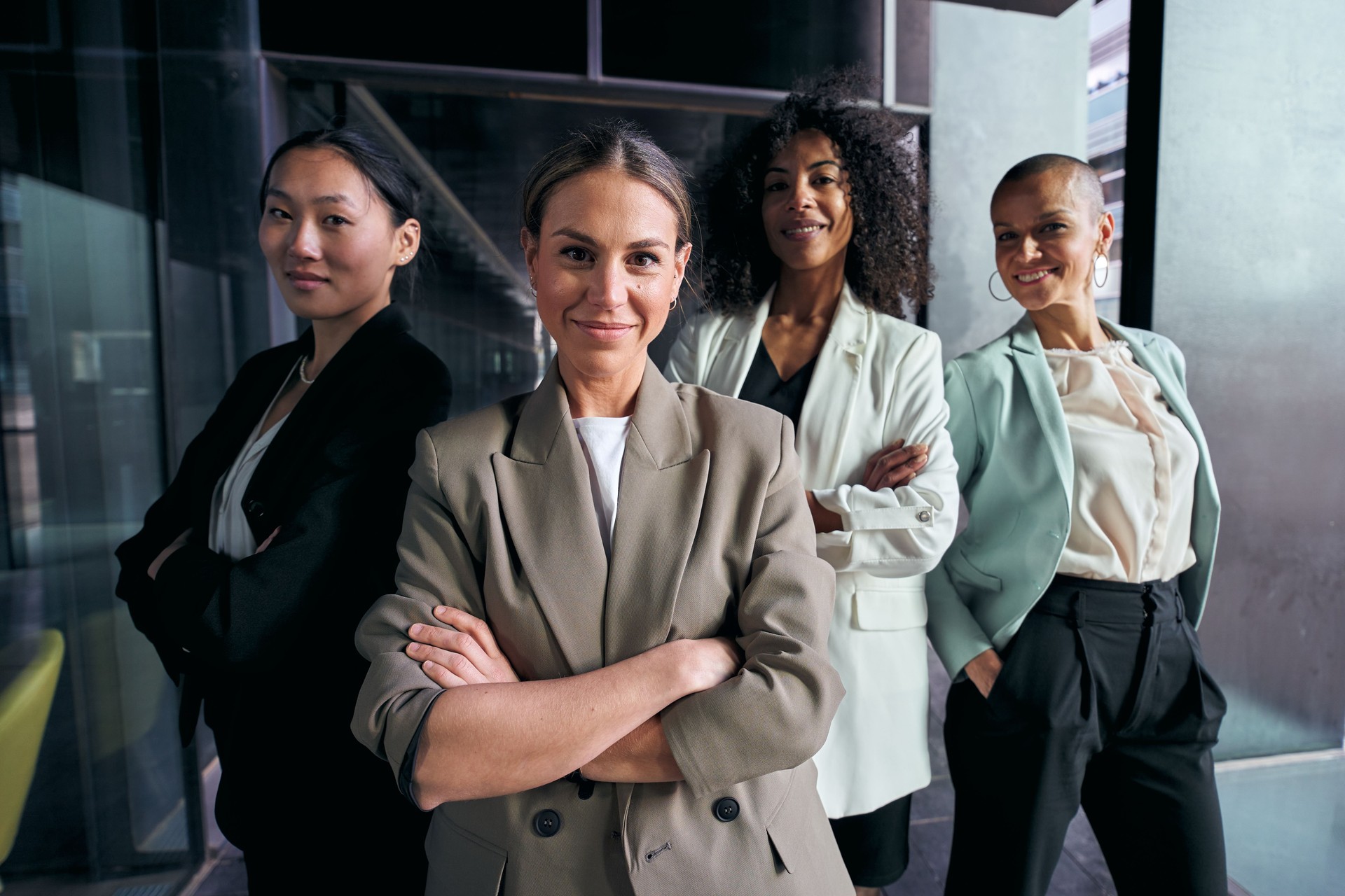 Group diverse attractive female professional in suits with arms crossed looking smiling at camera.